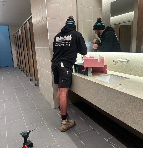 Commercial plumber performing hydraulic maintenance on restroom sink in Melbourne commercial building.