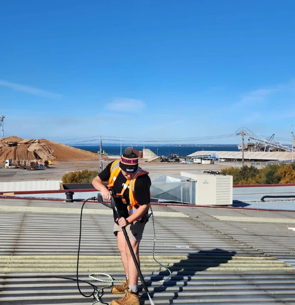 Professional exterior maintenance technician performing commercial roof repairs on Melbourne industrial building with safety harness.
