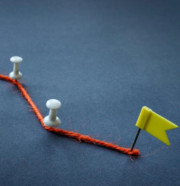 Red string marked by pins leading to a yellow flag, symbolizing milestones and achievement along a journey.